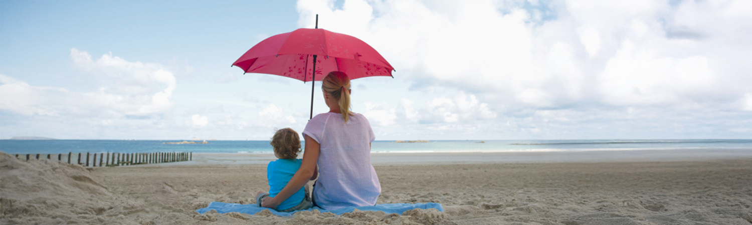 Mother and child on the beach with umbrella looking across the water